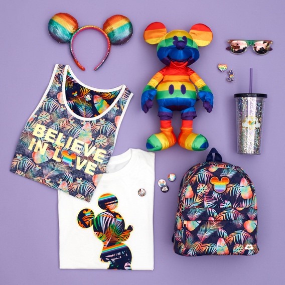 Photograph of the items in Disney Store UK's Rainbow Mickey Collection, including a t-shirt, vest, badges, backpack, plastic drinks cup and rainbow Mickey Mouse soft toy